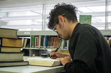 Joven universitario con gafas y piercing estudiando en la biblioteca	