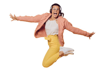 Excited brunette girl in glasses jumping, listening music in headphones spread out her arms dressed in yellow pants, white shoes, pink sweater and headphones on her head over transparent background.