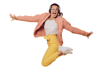 Excited brunette girl in glasses jumping, listening music in headphones spread out her arms dressed in yellow pants, white shoes, pink sweater and headphones on her head over transparent background.