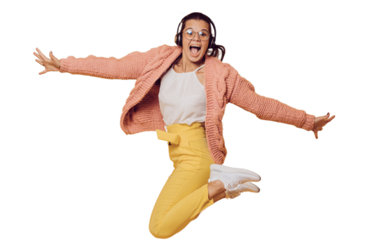Excited brunette girl in glasses jumping, listening music in headphones spread out her arms dressed in yellow pants, white shoes, pink sweater and headphones on her head over transparent background. - Powered by Adobe