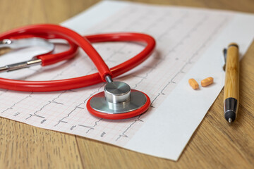 close-up of red stethoscope on electrocardiogram (ECG) paper, on the right pills and a bamboo pen