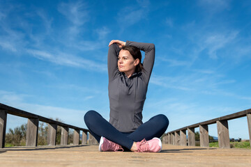 Sporty woman sitting cross legged doing an arm stretch warm up exercise.