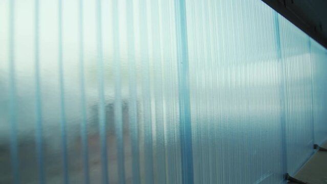 Wide wall of light blue colour made with translucent polycarbonate panels. Sheets of tough polymer plastic connected by reinforcing profiles closeup
