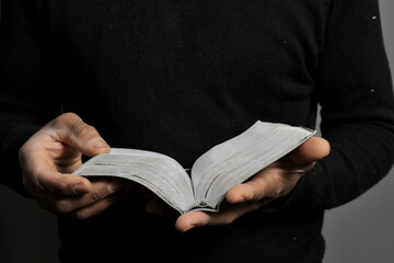 praying to God with hands on bible together with cross on grey black background with people stock photo