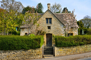 Quaint stone house in the Cotwolds of England with hedge and flowering trees in springtime
