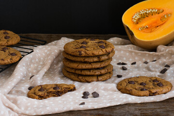 Galletas de calabaza con pepitas de chocolate sobre tela, mesa de madera y fondo negro. 