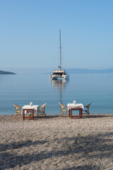 .Restaurant tables on the beach with a Catamaran moored in Bodrum harbor, a popular sailing and cruise destination along the Aegean coast in south west Turkey