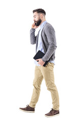 Side view of business man walking, carrying tablet and talking on the cellphone. Full body length portrait isolated on transparent background.
