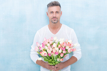 man with spring tulips in studio. man with spring tulips isolated on blue background.