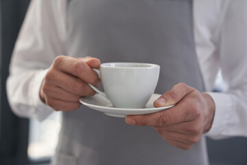 Your coffee, please. Cropped image of a man holding a cup of good coffee against the background of a window with space to copy. High quality photo