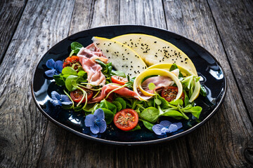 Tasty salad - prosciutto crudo, melon and fresh vegetables on wooden table
