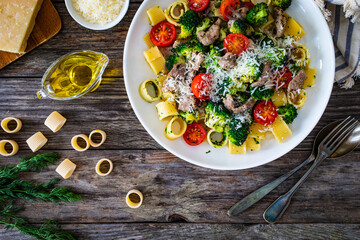 Pasta with roasted pork loin, broccoli, parmesan and cherry tomatoes on wooden table
