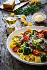 Pasta with roasted pork loin, broccoli, parmesan and cherry tomatoes on wooden table