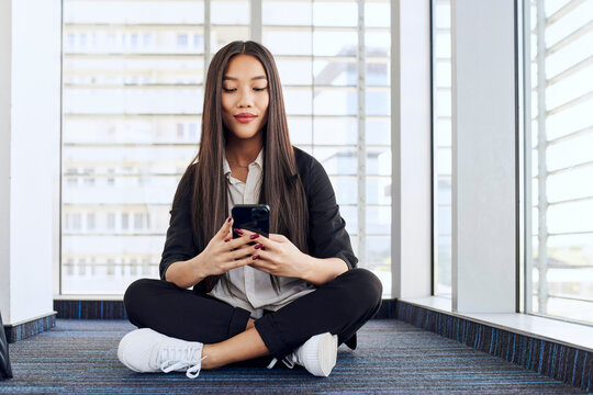 Young business woman sitting on the floor at modern office using mobile phone