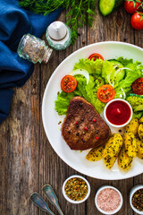 Fried beef sirloin with potatoes and vegetables on wooden table
