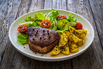 Fried beef sirloin with potatoes and vegetables on wooden table
