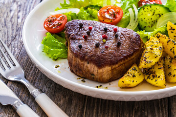 Fried beef sirloin with potatoes and vegetables on wooden table
