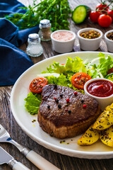 Fried beef sirloin with potatoes and vegetables on wooden table
