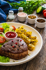 Fried beef sirloin with potatoes and vegetables on wooden table
