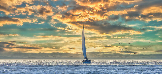 Sailboat sailing towards the horizon at sunset