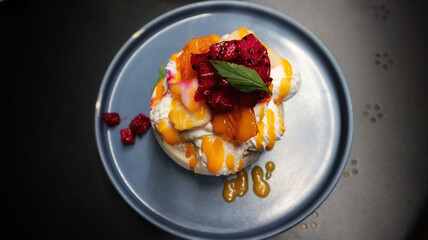 Pavlova serve in a blue plate a meringue dessert usually topped with strawberry and orange fruit and whipped cream.