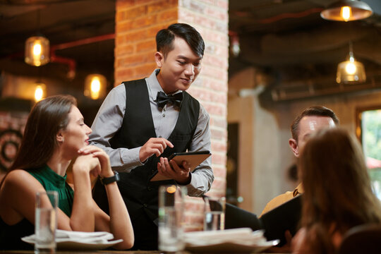 Smiling restaurant waiter taking order from family