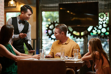 Fancy restaurant waiter showing customer bottle of good red wine