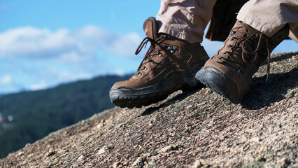 Vista de piernas y botas de hombre en una roca en lo alto de la montaña con vistas a un valle