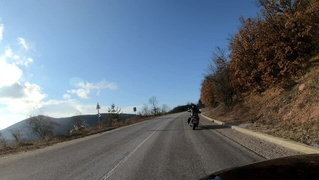 Man in black leather jacket riding a motorcycle on the road across the mountain