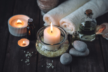 Spa setting with essential oil, candle, sea salt, pebbles, towel on dark wooden background. Massage, aromatherapy. Natural organic ingredients for relaxation, detention. Wellness in salon concept