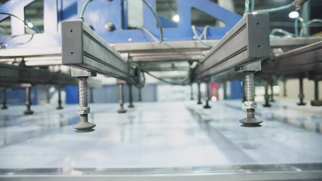 Transparent sheet of polycarbonate moves along conveyor belt. Manipulator with vacuum suction cups takes and lifts sheet up at modern factory closeup