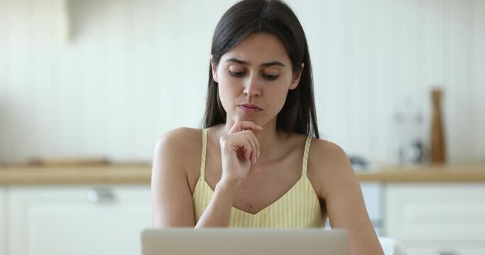 Pensive serious woman typing on laptop sit at table in kitchen, do telework, freelance job from home using internet and modern wireless technology, thinks, ponder over task studying online, close up