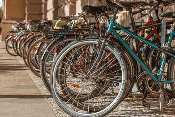 Fototapeta na wymiar Vintage retro bicycles wheels parked in a row in a bike parking lot on a city street during the day. Eco-friendly two-wheeled transportation. Travel, outdoor activity concept. Means of transportation.
