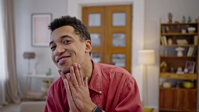 Young African man looks at camera as in mirror, fixes hair and strokes chin, enjoys his appearence