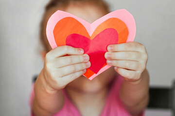 DIY holiday card with a red paper heart, a symbol of love. child holding homemade paper cut hearts Mother's Day, Valentine's Day