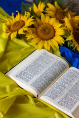 Bible (Holy Writ) and sunflowers on background of flag of Ukraine.