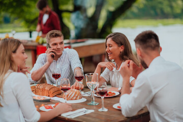Group of happy friends having picnic french dinner party outdoor during summer holiday vacation near the river at beautiful nature