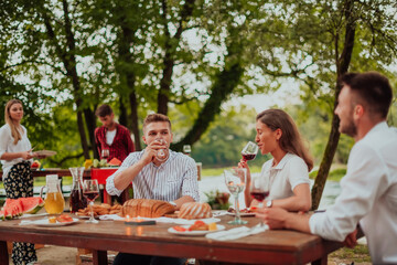 Group of happy friends having picnic french dinner party outdoor during summer holiday vacation near the river at beautiful nature