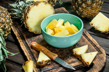 Pieces of ripe pineapple in a bowl on a cutting Board with a knife.