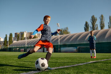 Boy playing football on field and kicking soccer ball
