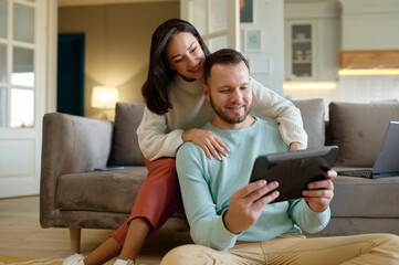 Happy young family couple using mobile tablet at home together