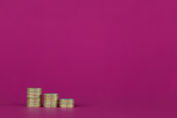 Three growing stacks of UK sterling gold color coins placed to the left of a Fuchsia, bright purple, pink background with plenty of copy space.