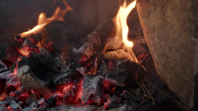 close up view of kindling for fire that lights up while lying on coals in nature. View of campfire in nature, smoke rises from fraying branches and coal.