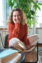 Happy pretty young positive woman sitting on chair relaxing at home looking at camera. Smiling...