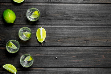 Vodka in a shot glass and lime slices.