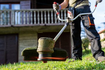 Worker with electric mower in his hands, mowing grass in front of the house.