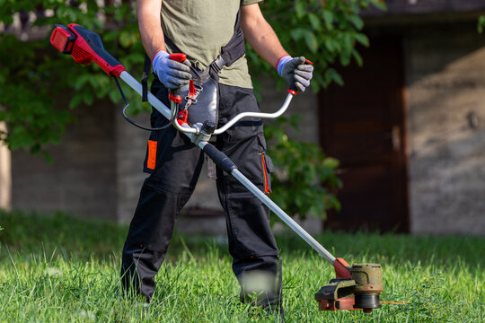 Landscape maintenance concept. Man cutting grass in yard by using electric string grass trimmer.
