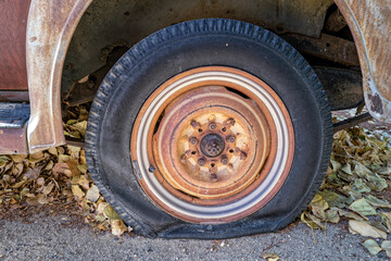 A flat tire on a rusty antique car