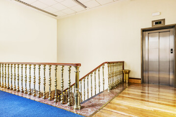 Elevator and stair area of a vintage building with hardwood floors and red marble steps
