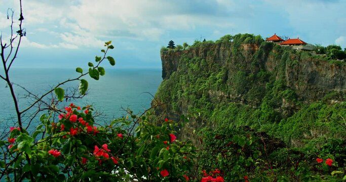 Ocean view and ancient religious monument on egde of cliff Uluwatu Temple on Bali Island. Indonesia. Flamboyant pink flowers.